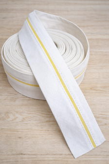 Witte pantalonband met gele antislip‑stiksel op lichte houten tafel &ndash; white trouser waistband with yellow anti&amp;#x