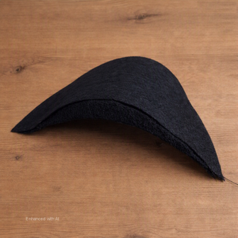 Zwarte vilten schoudervulling met zichtbare lagen in halve‑maanvorm op houten tafel &mdash; Black felt half‑moon