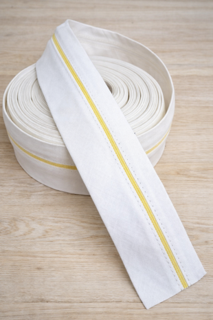 Witte pantalonband met gele antislip‑stiksel op lichte houten tafel &ndash; white trouser waistband with yellow anti&#x