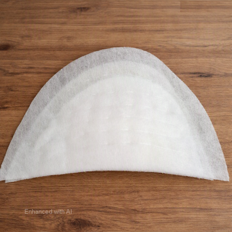 Witte vilten schoudervulling in halve‑maanvorm op houten tafel, bovenaanzicht met zichtbare lagen &mdash; White felt ha
